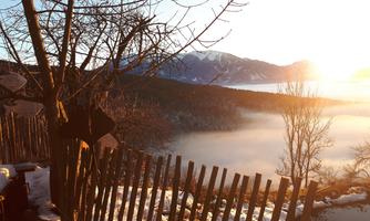 A picturesque view of a snowy landscape with mountains in the background. The sun rises and illuminates the fog over the valley.