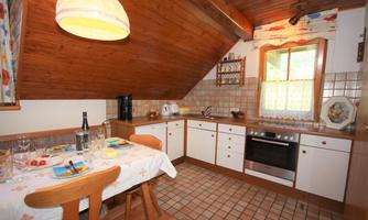 A cozy kitchen with a wooden ceiling and bright cabinets. The table is set, and the window offers a view of the greenery.