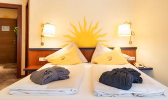 A cozy bedroom with two single beds and yellow pillows. On the wall is a sunny decoration that creates a friendly atmosphere.