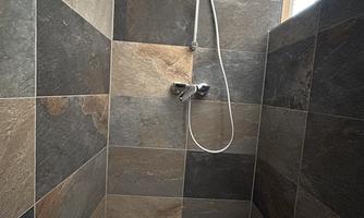 A modern shower with elegant slate-colored tiles. The faucet and shower head are designed to be simple and functional.