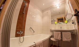 A modern bathroom with a bathtub and a shower. The room is bright and clean, featuring a sink and a mirror.
