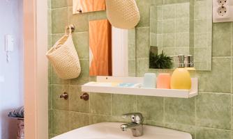 A modern bathroom with green tiles and a round sink. There are several mirrors and practical storage baskets.