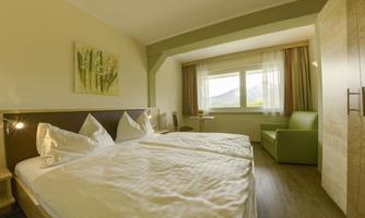 A cozy room with two beds and modern interior. Large window with a view of the surroundings and a green armchair in the corner.
