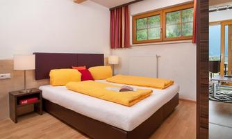 A bright bedroom with a large double bed and yellow pillows. The windows offer a view outside and let in plenty of daylight.