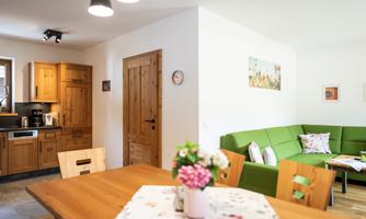 A cozy living space with a modern kitchen and a dining area. The green couch and the wooden table create an inviting atmosphere.