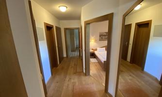 An inviting hallway with wooden flooring and several doors. Soft light and a mirror create a cozy atmosphere.