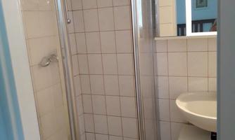 A small bathroom with a shower cubicle and a sink. The walls are tiled, and there is a mirror above the sink.