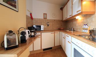 A modern kitchen with wooden shelves and white cabinets. On the countertop, there are various kitchen appliances such as a toaster and a coffee maker.