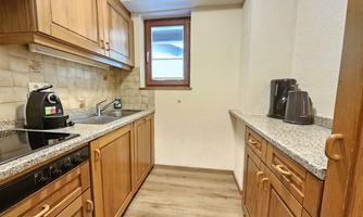 A modern kitchen with wood-colored cabinets and granite countertops. On the countertop, there is a coffee machine and a kettle.