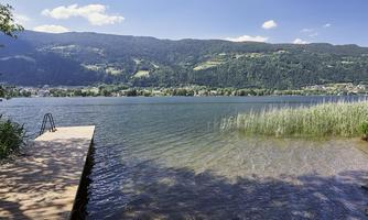 A peaceful lake with clear water and gentle waves. In the background, green hills and a bright blue sky can be seen.