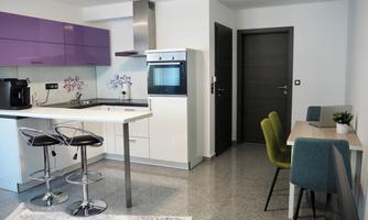 A modern kitchen with purple surfaces and elegant bar stools. The room also features a dining area with a table and chairs.