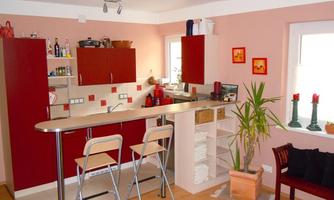 A modern kitchen with red cabinets and a small bar counter. The room features plants and decorative elements.