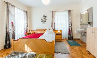 A modern bedroom with a large bed and light wood. The room has large windows that provide plenty of daylight.