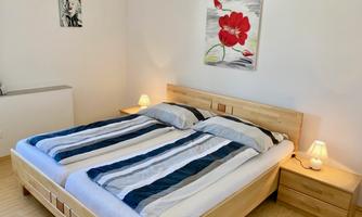 A modern bedroom with a double bed and striped bed linen. A colorful painting hangs on the wall and there are nightlights on the nightstands.