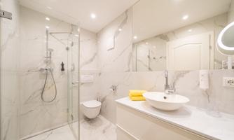 A modern bathroom with marbled walls and a glass shower. The sink is elegant, and there is bright lighting.