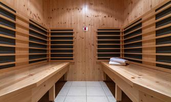 A bright sauna room with wooden paneling. In the center are two benches and a few folded towels.