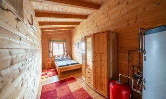 A cozy bedroom with wooden walls and a double bed. The room is bright and includes a wardrobe as well as a carpet.
