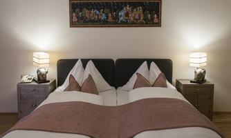 A cozy bedroom with two single beds and elegant pillows. Decorative pictures hang on the walls, and stylish nightstands with lamps stand next to the beds.