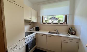 A modern kitchen with bright furniture and a window that offers a view of the outside world. There is a sink, a stove, and kitchen utensils on the countertop.