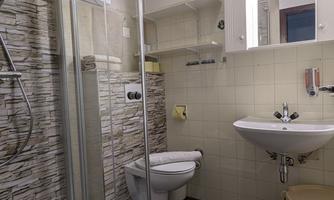 A modern bathroom with a glass shower and a hand washbasin. The walls are brightly tiled and the furnishings are functional.