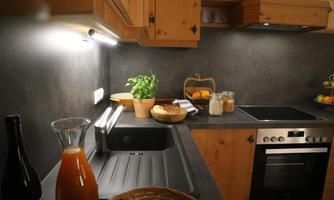 A modern kitchen with wooden shelves and dark countertops. On the countertop, there is a carafe, fruit, and a small plant pot.
