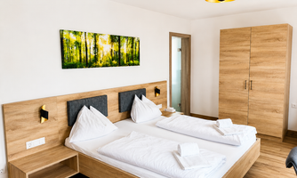 A modern bedroom with two single beds and wooden flooring. A vivid picture of a forest hangs on the wall.