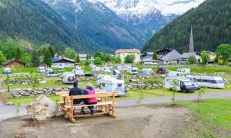 A peaceful campsite in a picturesque mountain landscape. In the foreground, two people are sitting on a bench, enjoying the view.