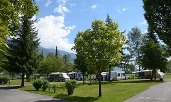 A campsite with several caravans and green trees. The sky is clear, and the surroundings are peaceful and inviting.