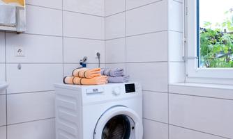 A modern washing machine stands in a bright laundry room. Neatly folded towels in various colors are placed on the machine.