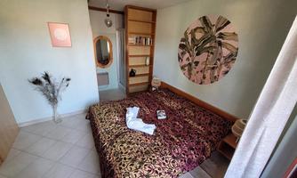 A cozy bedroom with a large bed and colorful pillows. On the wall hangs a round picture with plant motifs.