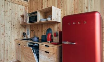 A modern kitchen with wooden paneling and a red SMEG refrigerator. The equipment includes a stove, a microwave, and a dishwasher.