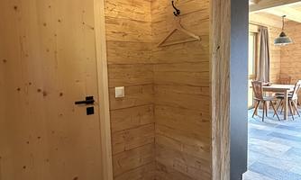 A cozy entrance area with wooden walls and a closed door. There is a hook for hanging as well as a view of the dining area.