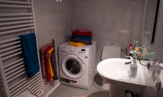 A modern bathroom with a washing machine and a sink. Colorful towels are stacked on the machine and more towels are hanging on the wall.