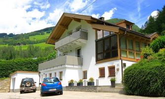 A modern house with a bright facade and large windows. In the background, green hills and a blue sky are visible.