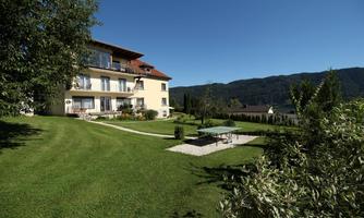 A beautiful house with several balconies, surrounded by green grass. In the foreground, there is a ping-pong table and expansive mountains in the background.
