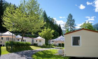 A peaceful campsite with mobile homes and sleeping tents amidst green nature. The sun is shining and the sky is clear.