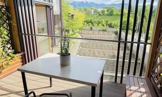 A cozy terrace with a table and a chair. In the background, green trees and a clear sky can be seen.