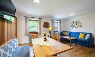 A cozy living room with modern furniture and a dining table. Large windows provide plenty of daylight and an inviting atmosphere.
