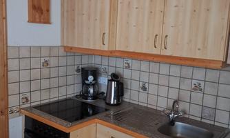 A small kitchen with wooden cabinets and modern appliances. It contains a stove, a sink, and a coffee machine.