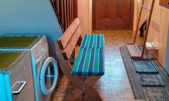A hallway with a washing machine, a bench, and a foosball table. The entrance door is visible, and there are wooden shelves on the walls.