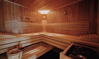 A cozy sauna room with wooden paneling and benches. On the floor, there is a bucket and a ladle.
