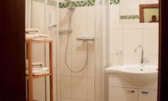 A modern bathroom with a shower cabin and a washing facility. On a shelf, handy towels are stacked.