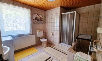 A modern bathroom with a shower and a large window. The room features bright tiles and a cozy wooden ceiling.