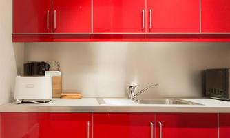 A modern kitchen with shiny red cabinets. On the countertop are a toaster and a coffee machine.