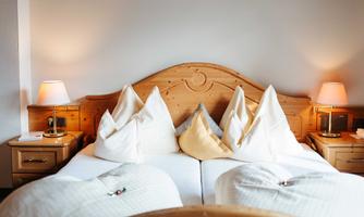 A cozy bedroom with a wooden bed and two elegant pillows. The soft lighting creates a relaxed atmosphere.