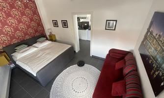 A modern room with a large double bed and a red sofa. The walls are decorated with a stylish pattern and the floor is tiled.