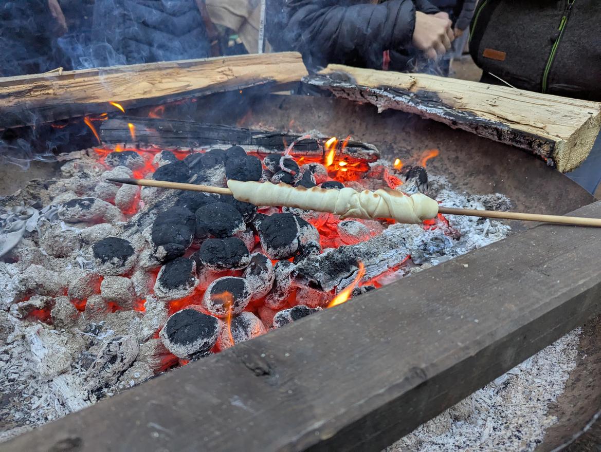 Stockbrot wird über glühender Kohle am Lagerfeuer gebacken, Rauch steigt auf