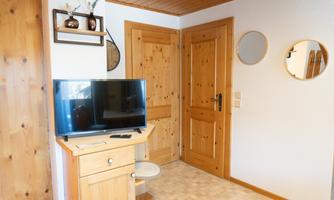 A cozy room with bright wood decor. A TV is on a small table, while a door and round mirrors can be seen on the wall.