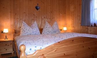 A cozy bedroom with a wooden bed and heart-shaped pillows. The walls are made of wood, and there is soft lighting from bedside lamps.