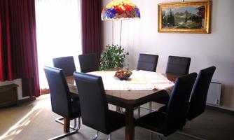 An elegant dining area with a large table and black chairs. A colorful lamp hangs above the table and a piece of artwork is on the wall.